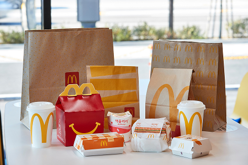 다양한 맥도날드 종이 포장재와 컵, 해피밀 상자가 진열된 모습으로, FSC 인증 친환경 종이 사용을 강조한 이미지.